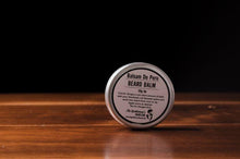 Round beard balm tin with white product label standing upright on a wooden surface