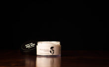 Transparent tub of hair wax with black lid in the background