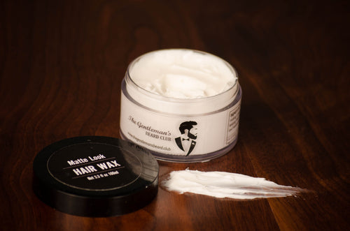 An open tub of hair wax containing a white substance and a smudge of white on the wooden surface