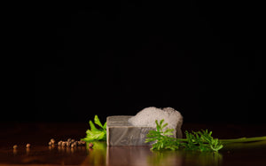 Grey bar of shave soap along green leaves and peppercorn next to it