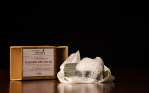 Grey bar of shave soap with foam on top and an open box at an angle in the background