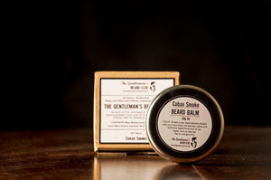 Round beard balm tin with white label and brown box in the background