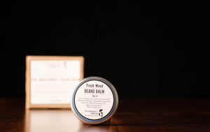 Round stainless steel beard balm tin with a white label and a brown box in the background