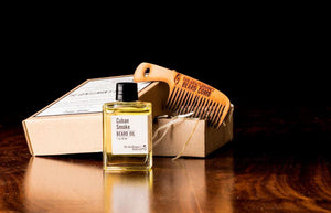Clear beard oil bottle of yellow oil enclosed with a black cap with a comb and box in the background