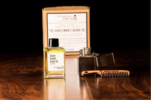 Glass beard oil bottle filled with beard oil and a silver lighter and comb alongside