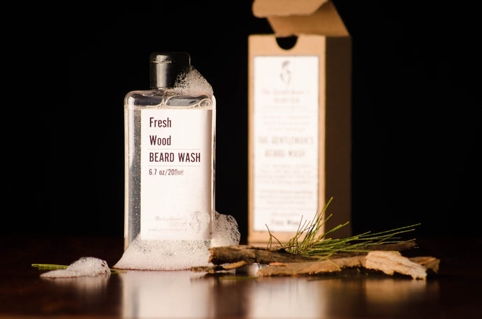 Transparent beard wash bottle with black cap and an open box in the background