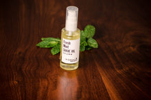 Transparent bottle of shave oil in front of green mint leaves on a wooden table