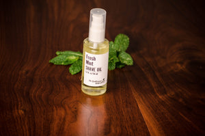 Transparent bottle of shave oil in front of green mint leaves on a wooden table