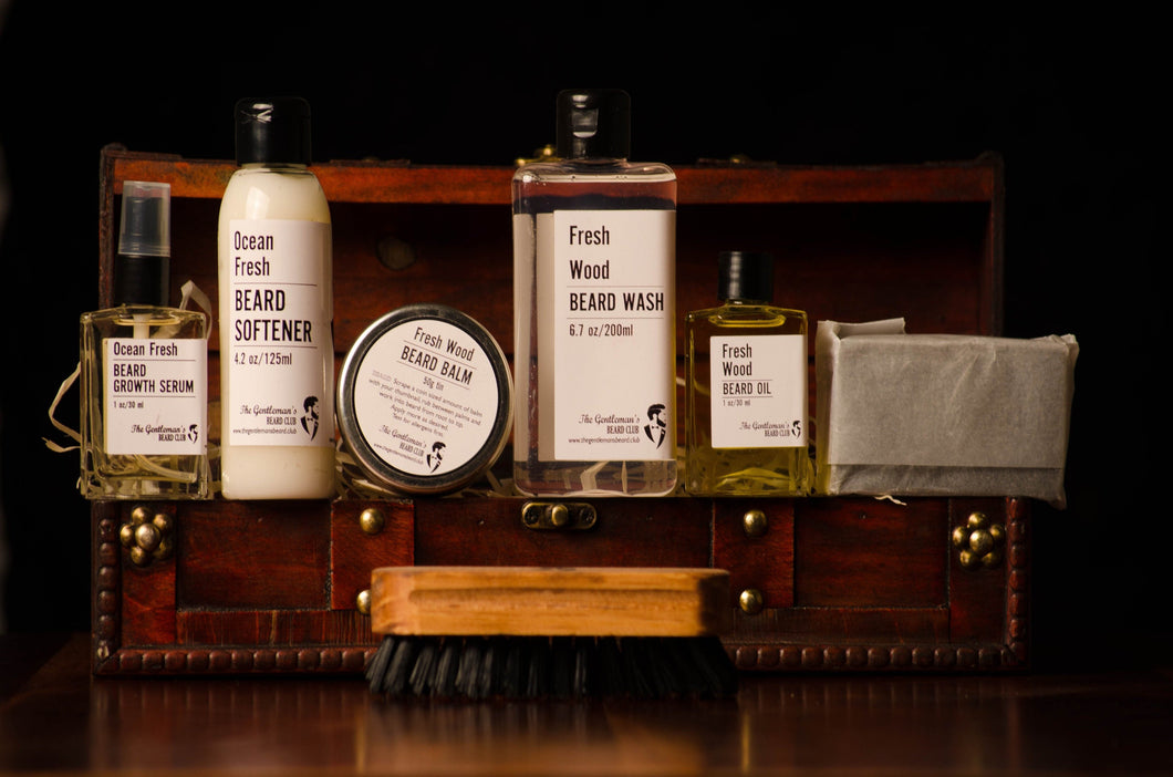 Beard grooming kit items lined up in front of a wooden treasure chest in the background